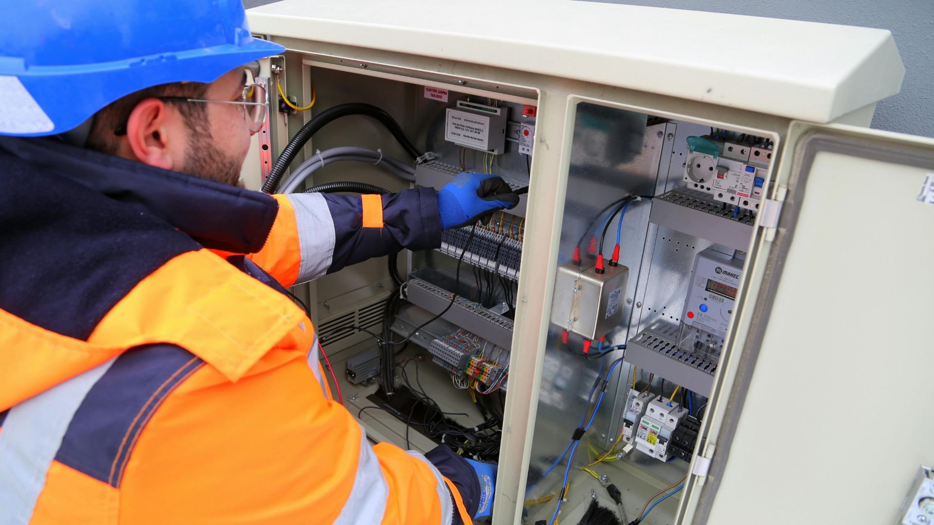 Electrician in safety gear checking electrical control panel with wiring