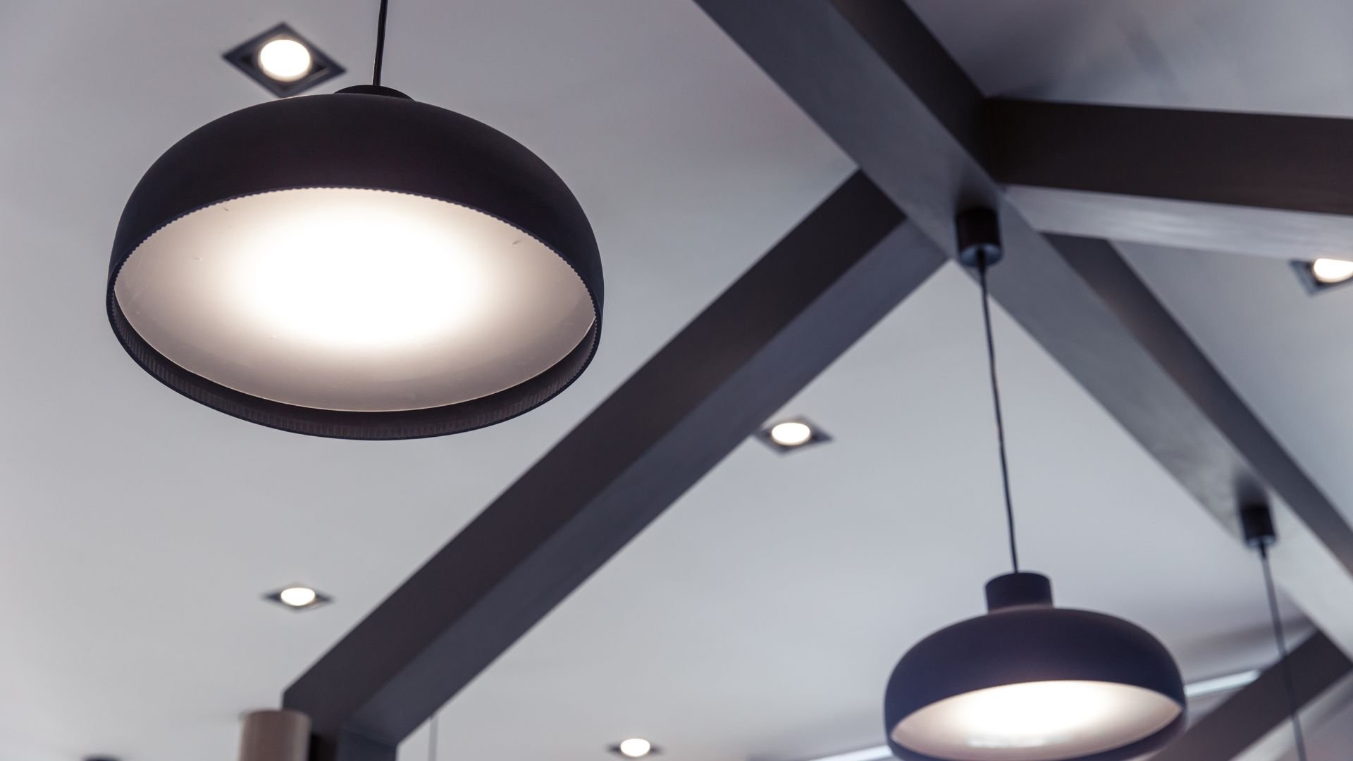 Modern black pendant lights hanging from geometric ceiling with recessed spots