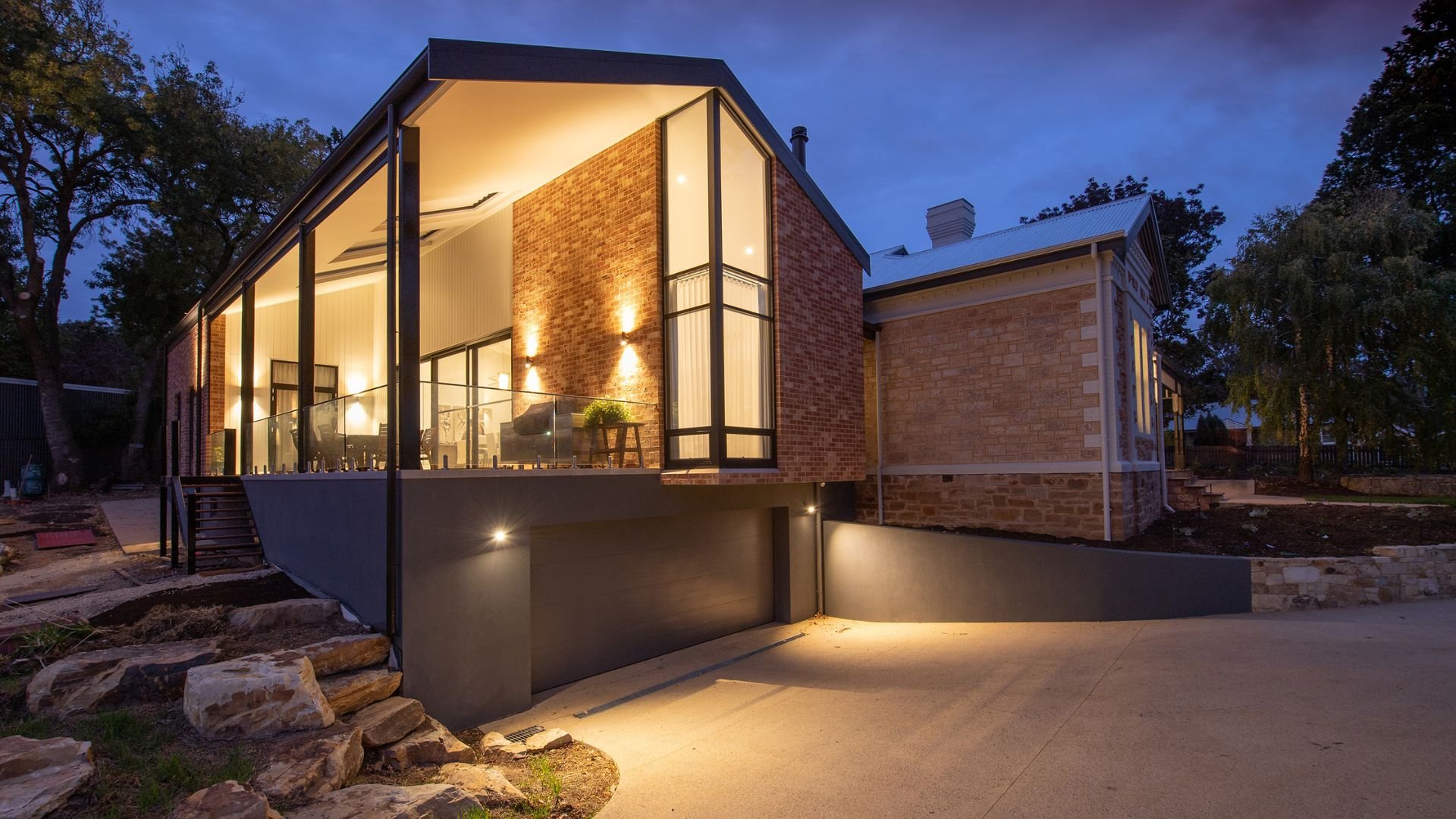 Modern brick and glass house illuminated at dusk with landscaped surroundings
